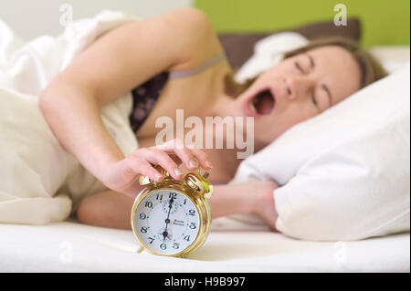 Giovane donna sbadigli nel letto, sveglia squilla Foto Stock