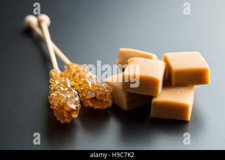 Lo zucchero di canna cristalli sulla memory stick e caramello caramelle su sfondo nero. Foto Stock