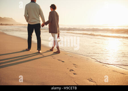 Vista posteriore di una coppia senior camminando lungo la riva del mare. Uomo maturo e la donna insieme a passeggiare sulla riva del mare al tramonto. Foto Stock