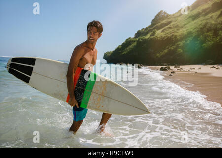 Colpo di bel giovane con le tavole da surf sulla spiaggia. Voce maschile proveniente dal mare dopo che l'acqua surf. Foto Stock
