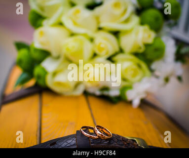 Gli anelli di nozze giacente su un giallo pezzo di legno con rose bianche su uno sfondo Foto Stock