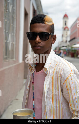 Ritratto verticale di un giovane cubano con striature bionde tinte nei capelli e molti piercing facciali con occhiali da sole Foto Stock