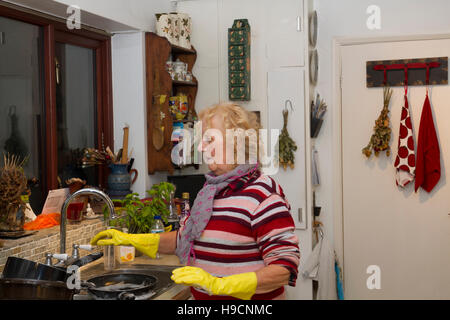 In piedi al lavello lavando a mano, donna che indossa guanti di gomma facendo le stoviglie, lavando i compiti. Foto Stock