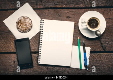 Pagina vuota di notepad sul tavolo di legno, miele-torta, smartphone, penna e matita e tazzina di caffè Foto Stock