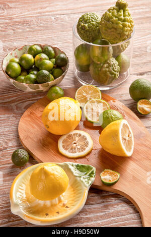 Lime e limone con strizzatore sul tavolato in legno Foto Stock