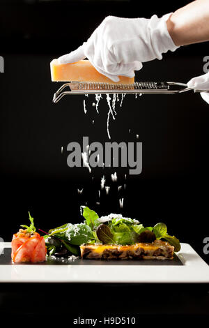 Lo Chef grattugiare formaggio su insalata con sfondo nero Foto Stock