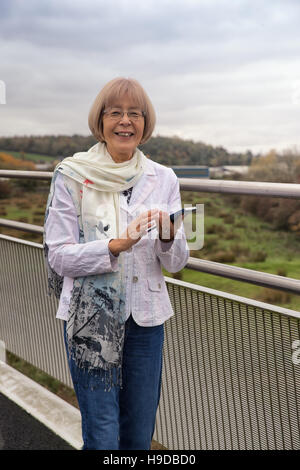 Anziani donna giapponese utilizzando uno smart phone e sorridente Foto Stock