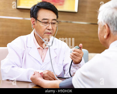 Asian medico la misura della pressione del sangue di un paziente senior dello sfigmomanometro utilizzando Foto Stock