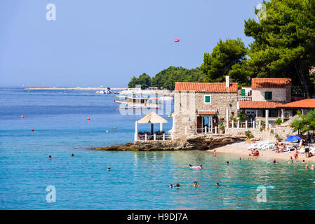 Bol, Croazia - 7 Luglio 2016: Beach Bar & Restaurant Ribarska kucica in Bol, isola di Brac. Famosa spiaggia di Zlatni rat in background Foto Stock