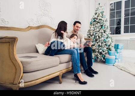 Famiglia allegra in salotto divertendosi con la tavoletta digitale che Babbo Natale ha portato la sua, dietro l'albero di Natale decorato Foto Stock