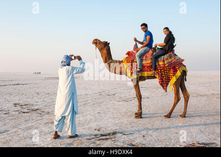 Una guida locale a fotografare i turisti su un cammello nel grande rann di Kutch, un sale stagionale marsh situato nel deserto di Thar di Gujarat, India. Foto Stock