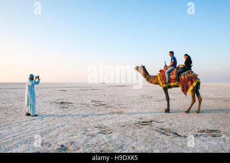 Una guida locale a fotografare i turisti su un cammello nel grande Rann di Kutch, un sale stagionale marsh situato nel deserto di Thar di Gujarat, India. Foto Stock