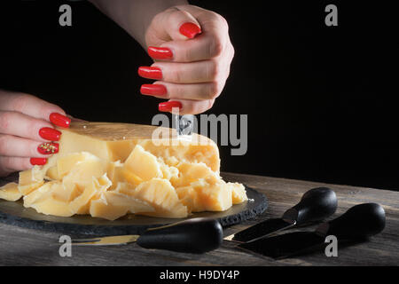 Mani femminili con luminosi bella manicure rompere i pezzi di formaggio a pasta dura come parmigiano per mezzo di un coltello speciale Foto Stock