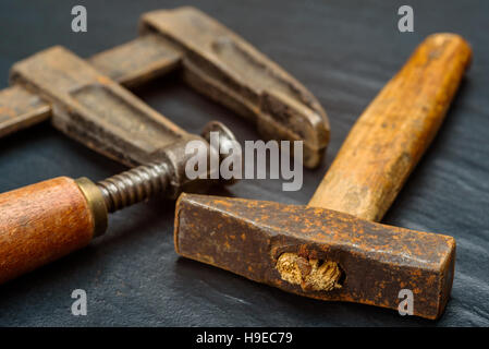 Vecchio e ben utilizzati a mano martello quadrato corto con manico in legno e il lato morsetto a vite su sfondo scuro. Foto Stock