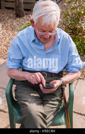 Un uomo nella sua 80's utilizzando uno smart phone nel Regno Unito Foto Stock