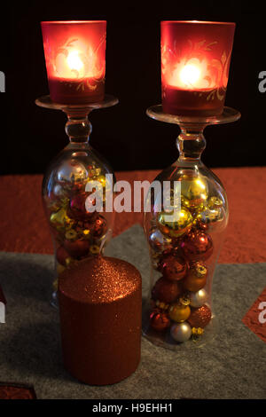 2 bicchieri da cocktail riempiti con coloratissime palle di Natale su un livello di grigio a forma di stella trivet, decorata con una candela rossa. I bicchieri da cocktail sono ruotati aro Foto Stock