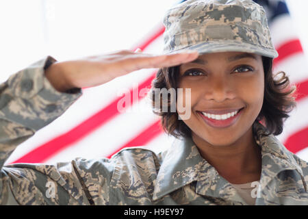 Ritratto di sorridere razza mista soldato salutando vicino a bandiera americana Foto Stock