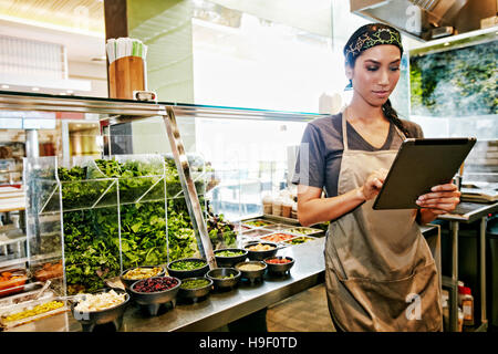 Razza mista food court lavoratore utilizzando tavoletta digitale Foto Stock