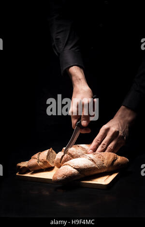 Close up di chef mani baguette di trinciatura su sfondo nero Foto Stock