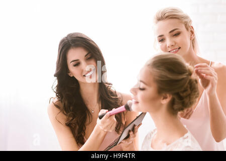 Felice bridesmaids aiutando la sposa per ottenere pronto Foto Stock