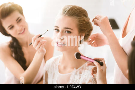 Piacevole giovane bridesmaids aiutando la sposa per ottenere pronto Foto Stock