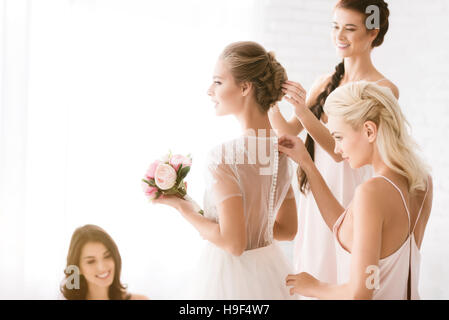 Felice bridesmaids aiutando la sposa per ottenere pronto Foto Stock