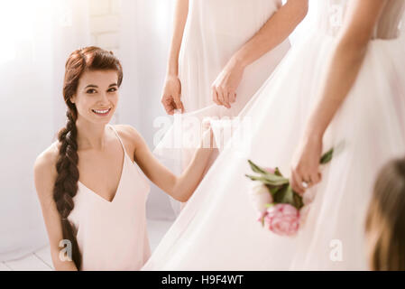 Sorridente giovane damigella aiutando la sposa per ottenere pronto Foto Stock