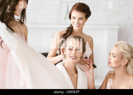 Felice bridesmaids aiutando la sposa per ottenere pronto Foto Stock