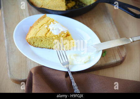 Cornbread cuneo con il burro con la padella in ghisa in background Foto Stock