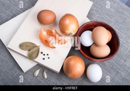 Vista superiore della tavola con materie prime per alimenti naturali in stile vintage - uova, cipolle, aglio e spezie su sfondo tessili Foto Stock