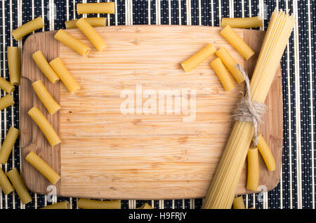 Vista dall'alto su una tabella con una tavoletta di legno, spaghetti e pasta per la cottura su sfondo a strisce Foto Stock