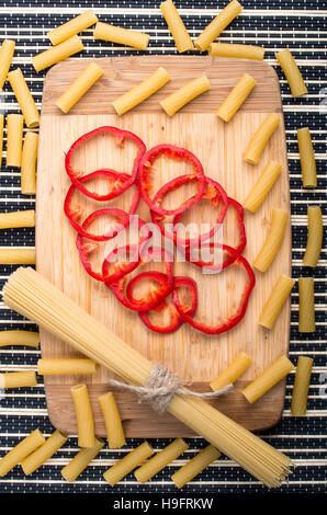 Vista verticale su sfondo di cibo da pasta e campana rosso-peperone per una sana cottura su una base di legno su uno sfondo a strisce Foto Stock
