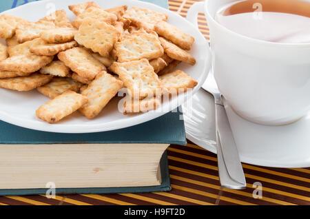 Vista da vicino su una tazza di tè e crackers a secco su un vecchio libro Foto Stock