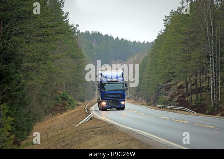 Blue semi carrello procede in salita lungo la strada rurale affiancata da foresta verde. Foto Stock