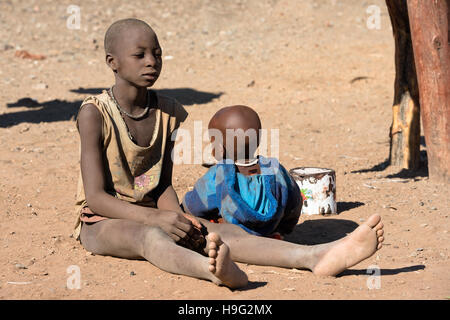 I bambini indigeni delle tribù Himba in abiti tradizionali stanno giocando nella sabbia al Kunene Regione della Namibia Foto Stock