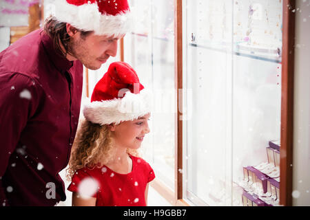 Immagine composita della vista laterale del padre e figlia in abito di natale guardando il display di gioielli Foto Stock