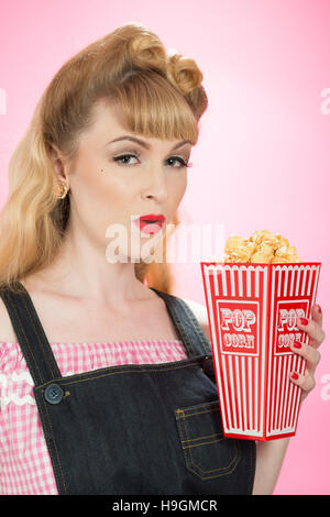 Pin up girl con scatola in cartone su popcorn su un brillante sfondo rosa Foto Stock