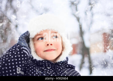 Ritratto di una incantevole piccola ragazza in un parco innevato durante una nevicata. Foto Stock