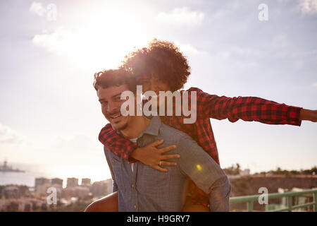 Giocoso amare giovane gesticolando aereo con il suo braccio sinistro fuori e tenendo premuto sul suo petto con il suo braccio destro mentre ottenere un piggy back ride Foto Stock