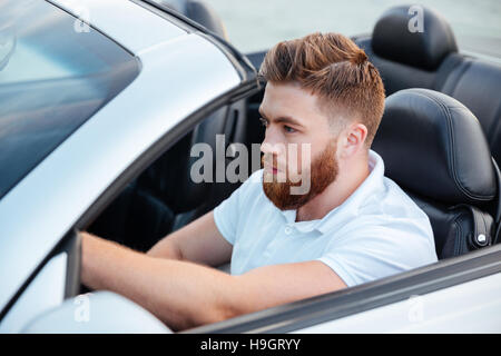 Bel giovane uomo barbuto alla guida della sua auto cabriolet Foto Stock