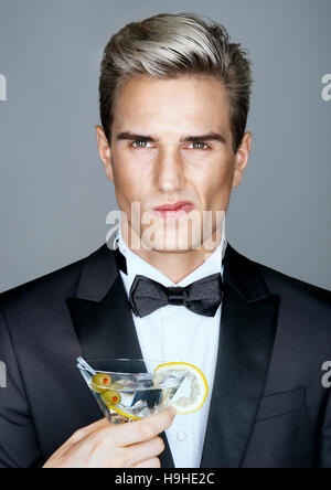 Scontento uomo ricco con un bicchiere di martini. Foto di uomo elegante in elegante abito nero. Vita alta Foto Stock