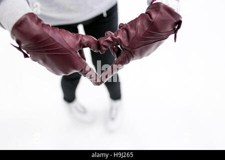 Primo piano della ragazza mostra astratto simbolo del cuore da guanti in pelle su ghiaccio. Concetto di amore per pattini, sport invernali. Foto Stock