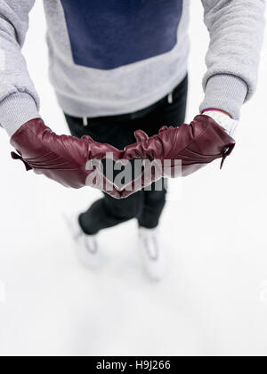 Vista superiore ragazza indossando pattini mostra astratto simbolo del cuore da guanti in pelle su ghiaccio. Concetto di amore per il pattinaggio e sport invernali. Foto Stock