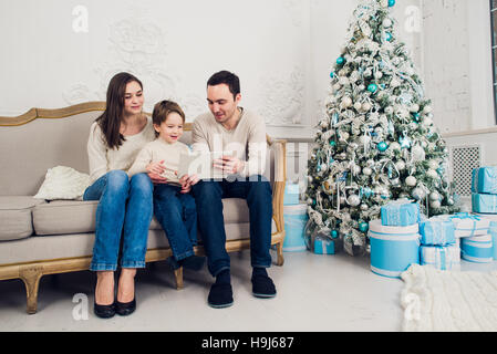 Famiglia allegra in salotto divertendosi con la tavoletta digitale che Babbo Natale ha portato la sua, dietro l'albero di Natale decorato Foto Stock