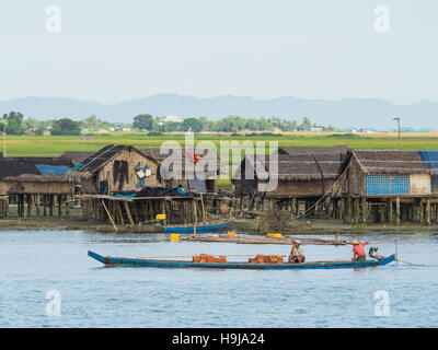 Trasporto in barca mattoni passando un piccolo villaggio lungo il fiume Kaladan in Stato di Rakhine, Myanmar Occidentale. Foto Stock