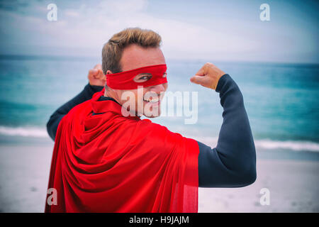 Uomo in costume da supereroe flettendo muscoli alla riva del mare Foto Stock