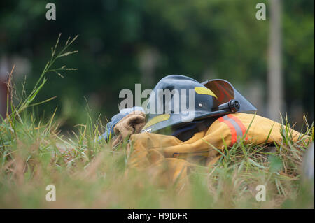 Per impieghi pesanti protettivo di lotta antincendio panno, guanti, casco, giacca, pantaloni su erba verde sullo sfondo Foto Stock