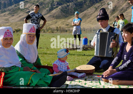 Nonne con il bambino e il padre a suonare la fisarmonica in abito tradizionale ad un picnic in soggiornare Kazakistan Foto Stock