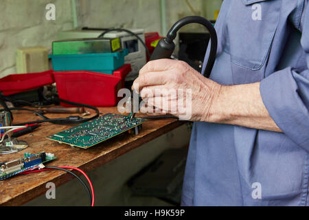 Lavoratore nel riciclo di computer impianto scheda madre di saldatura Foto Stock