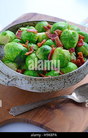 Freschi cotti al vapore cavolini di Bruxelles con pancetta croccante bit in screziato piatto di servizio. Colpo di luce naturale in formato verticale. Foto Stock